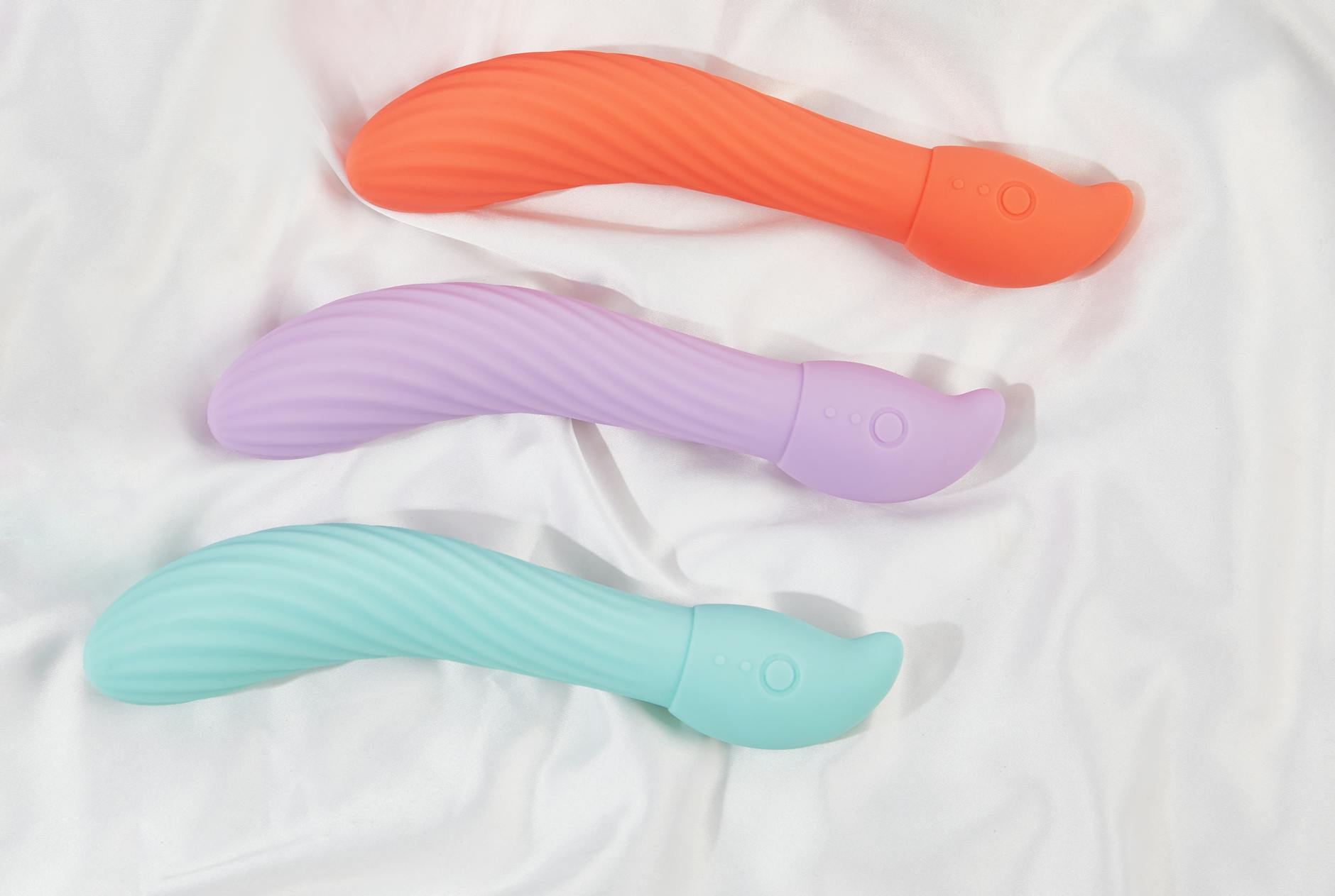 Trois vibromasseurs colorés arrangés sur du tissu blanc doux, mettant en évidence leur texture lisse et leur conception ergonomique.