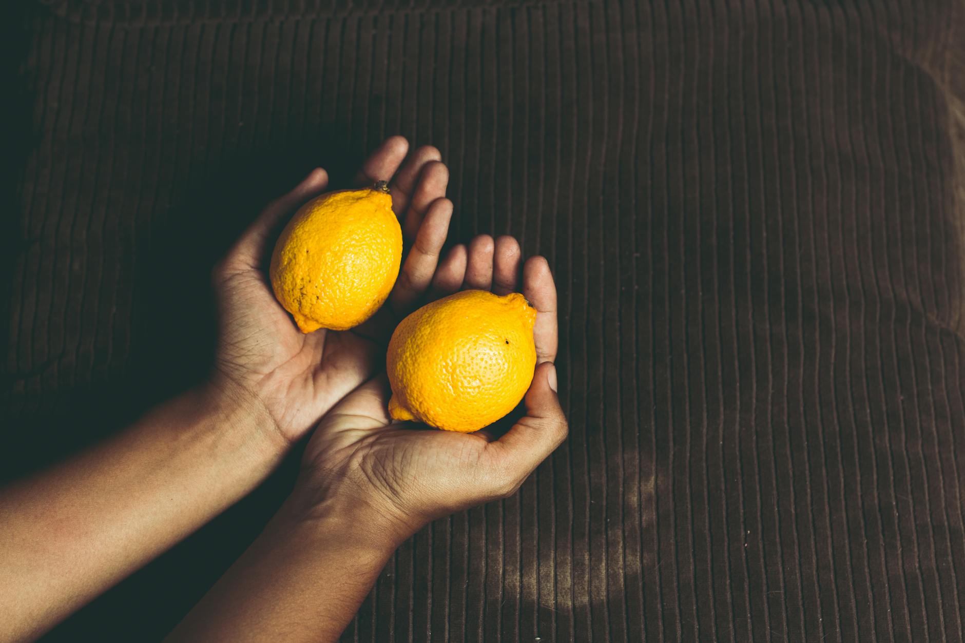 Deux citrons frais tenus dans des mains en coupe sur une surface marron, symbolisant la fraîcheur et le renouveau