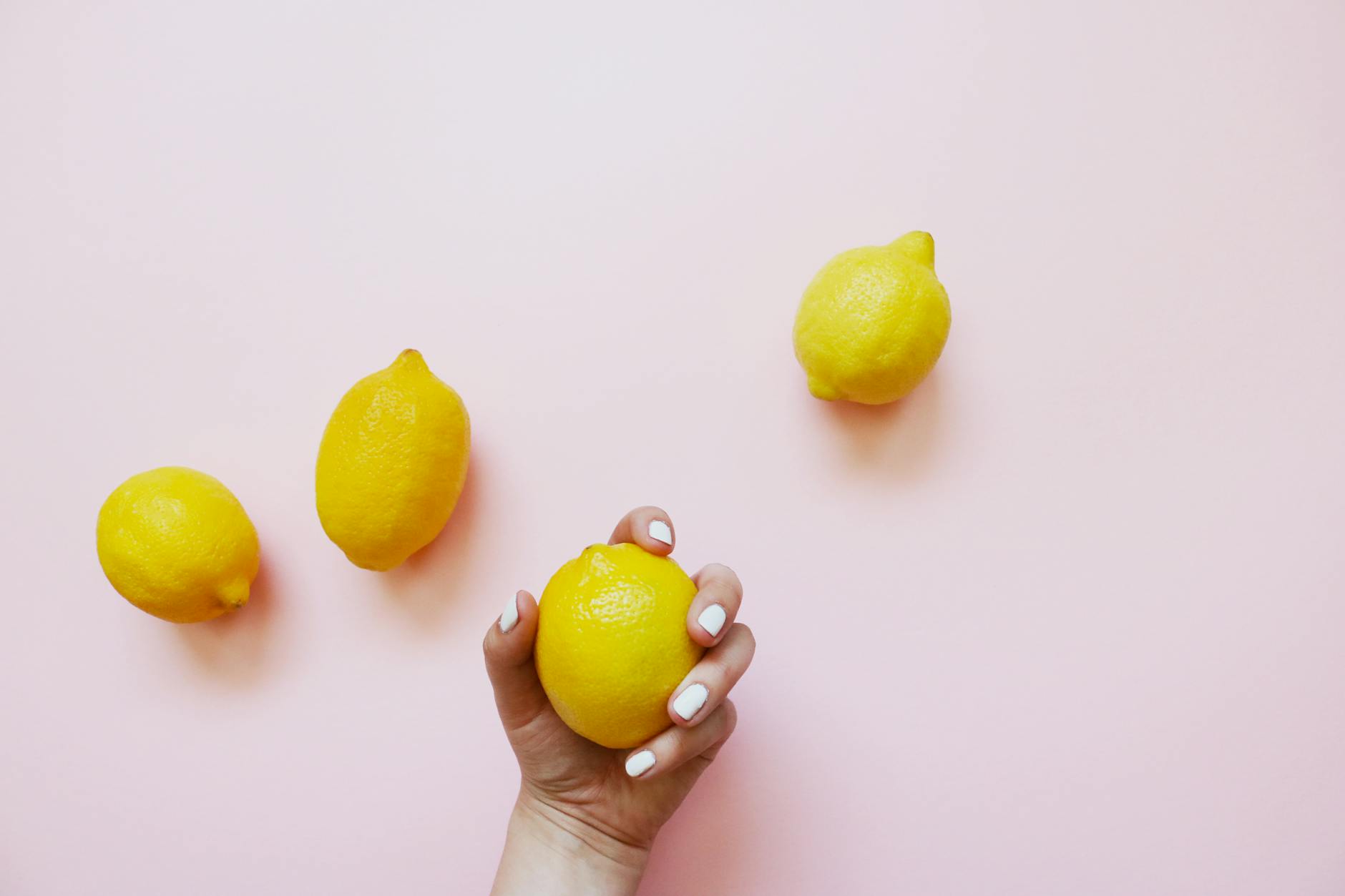 Une main tenant un citron jaune vif sur fond rose poudré, symbole de connexion naturelle et sensuelle