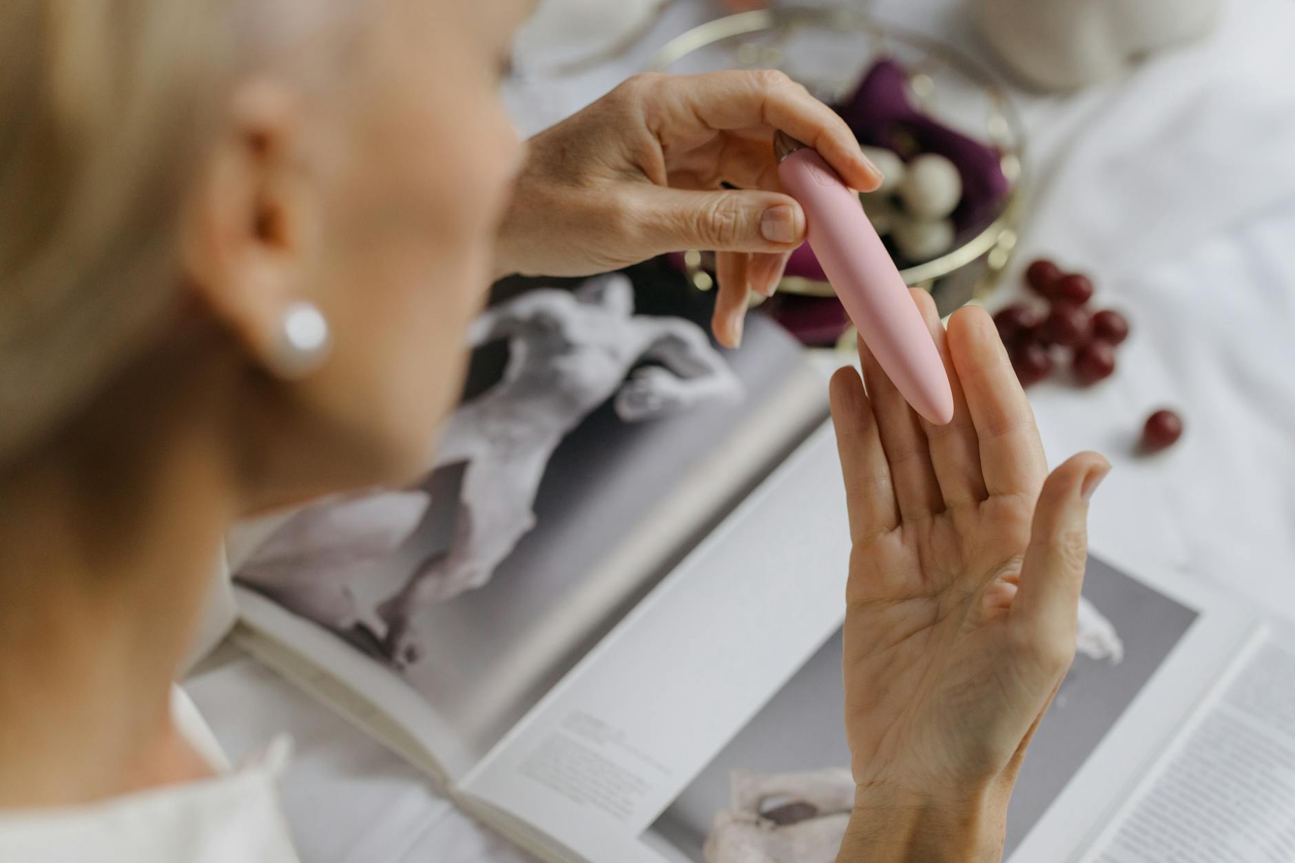 Close-up of hands holding a vibrator with art books in the background, emphasizing intimate personal themes.