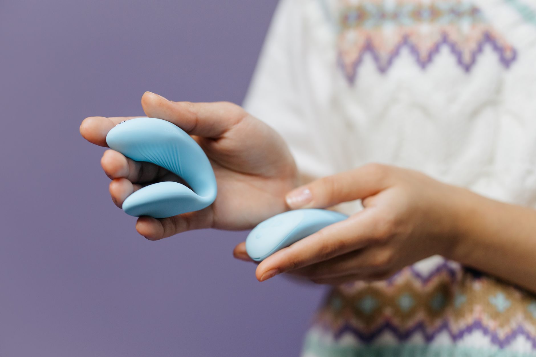 Mains tenant un vibromasseur bleu élégant contre un fond violet, représentant l'intimité et l'auto-plaisir