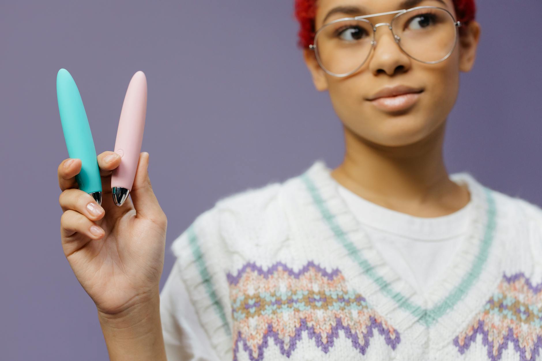 Femme tenant deux vibromasseurs colorés contre un fond violet, illustrant l'intimité et l'exploration sexuelle