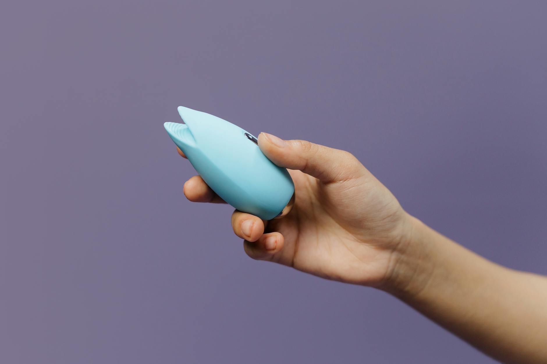 Un vibromasseur bleu silicone tenu dans une main sur fond violet, symbolisant l'acceptation du plaisir personnel