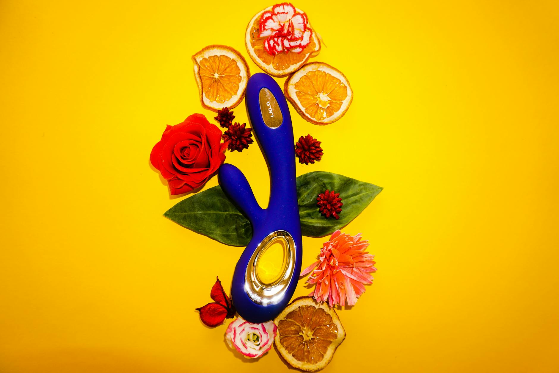 Vibromasseur bleu entouré de fleurs et de tranches d'orange sur fond jaune