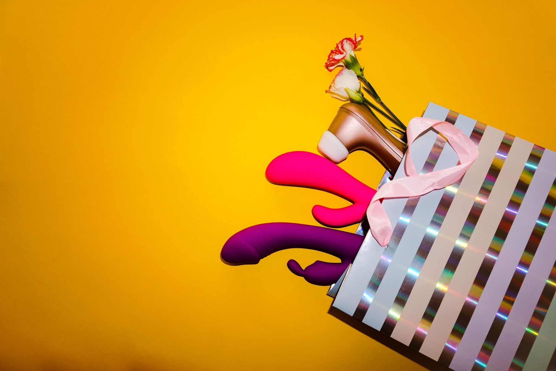 Vibromasseurs colorés avec fleurs dans un sac cadeau holographique sur fond jaune vif