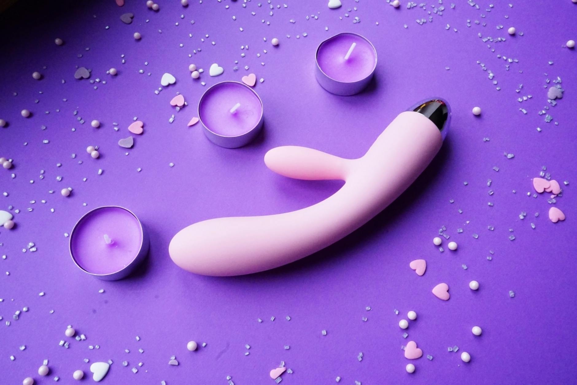 Vibromasseur rose sur fond violet avec confettis en forme de cœur et bougies pour une ambiance romantique